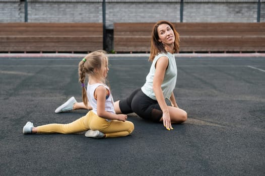 Mother and daughter go in for sports outdoors. Caucasian woman and little girl are engaged in fitness at the stadium