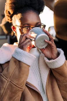 young black woman drinking a cup of a hot drink in a camper van at sunset, concept of van life and weekend getaway