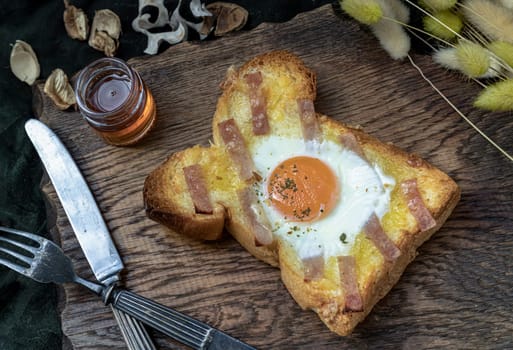Homemade fried egg in a hole Bacon and Cheese toast serve with Honey on wooden cutting board. Sandwiches for breakfast, The concept of delicious food, Selective Focus.