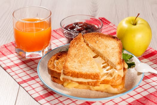 Toasted slices of bread with cheese and green parsley on white plate, glass og orange juice, apple and glass bowl with strawberry jam with red kitchen napkin. Good food for breakfast.