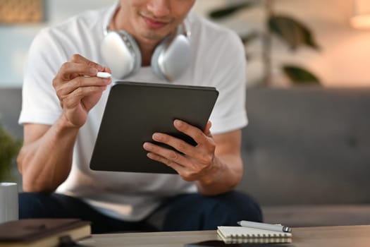 Smiling adult man in casual clothes sitting on couch and using digital tablet. Communication, technology and lifestyle concept.