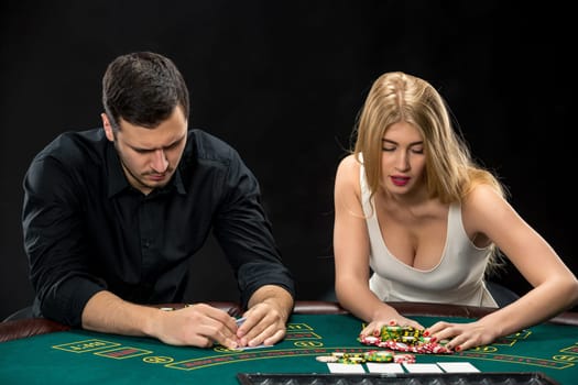 Two poker players sitting at a poker table on black background and going all-in pushing his chips forward