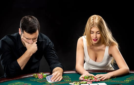 Two poker players sitting at a poker table on black background and going all-in pushing his chips forward