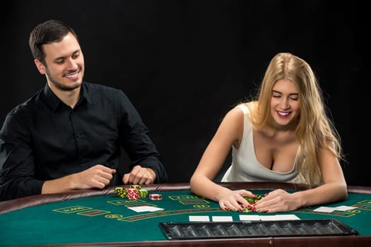 Young couple playing poker and have a good time in casino, woman taking poker chips after winning