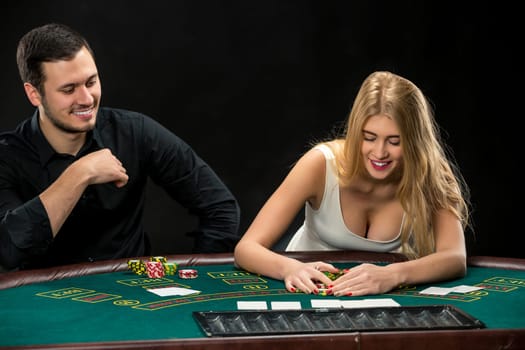 Young couple playing poker and have a good time in casino, woman taking poker chips after winning