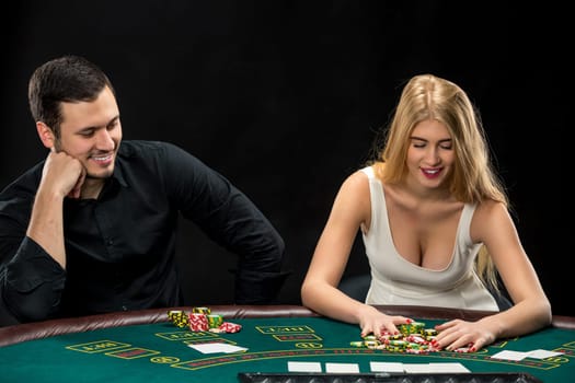 Young couple playing poker and have a good time in casino, woman taking poker chips after winning