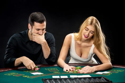 Young couple playing poker and have a good time in casino, woman taking poker chips after winning