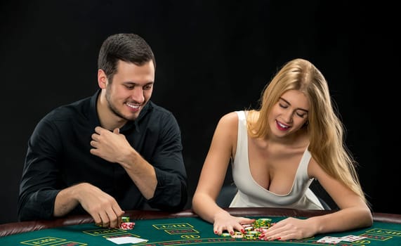 Young couple playing poker and have a good time in casino, woman taking poker chips after winning