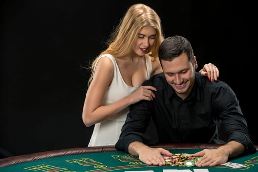 Young couple playing poker and have a good time in casino. Man taking poker chips after winning, woman embracing his