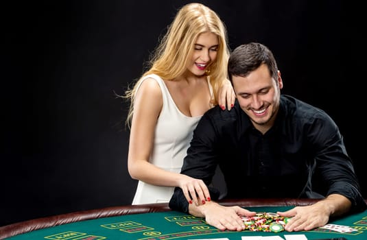 Young couple playing poker and have a good time in casino. Man taking poker chips after winning, woman embracing his