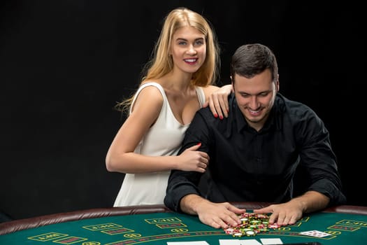 Young couple playing poker and have a good time in casino. Man taking poker chips after winning, woman embracing his