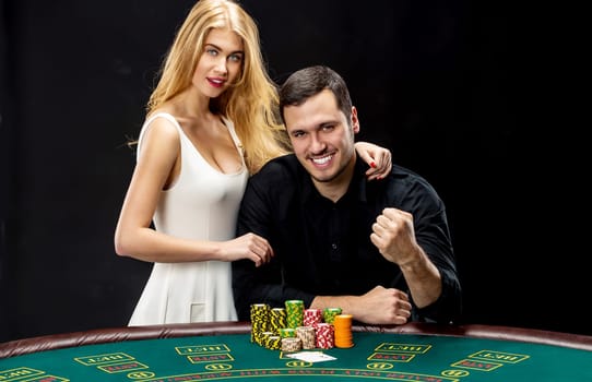 Young couple playing poker and have a good time in casino. Man taking poker chips after winning, woman embracing his