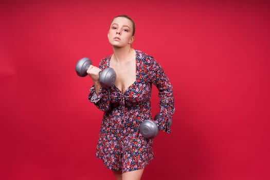 Beautiful model in sportswear with dumbbells looks at camera on yellow, red and dark background