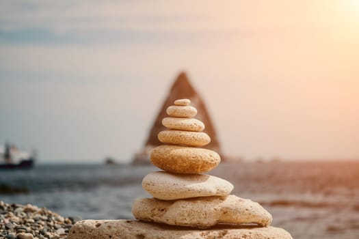 Pyramid stones on the seashore with warm sunset on the sea background. Happy holidays. Pebble beach, calm sea, travel destination. Concept of happy vacation on the sea, meditation, spa, calmness.