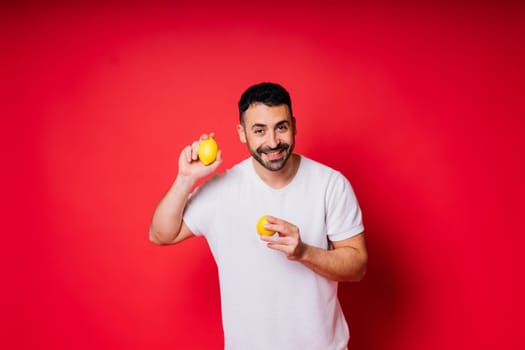 Portrait of young bearded man holding lemons in both hands on an isolated red background