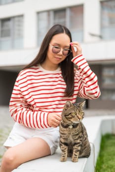 Young woman and tabby cat sitting on a bench outdoors