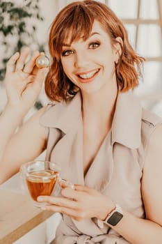 Woman drinks tea close-up. Portrait of a brunette in a beige dress with a transparent mug and a candy in her hands