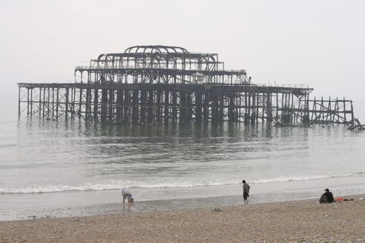 People on the pebble beach in front of the ruins of the West Pier in Brighton, Uk.