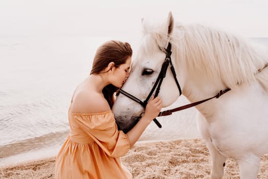 A woman in a dress stands next to a white horse on a beach, with the blue sky and sea in the background