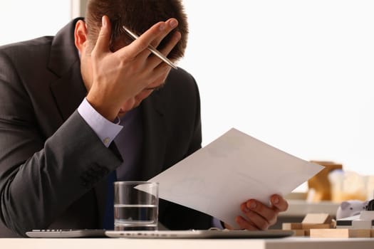 Stressed businessman with headache or migraine working at office desk. Bankruptcy depression and loan documents with debts