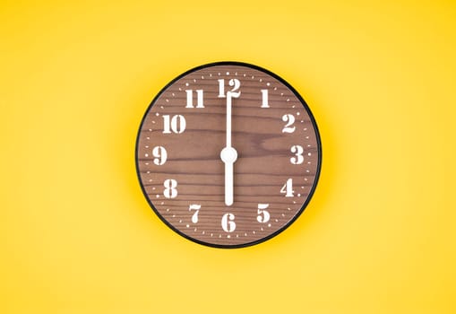 Retro wooden clock at 6 O' clock on yellow color background.