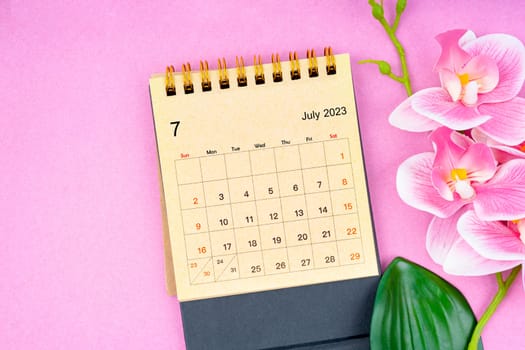 July 2023 calendar desk and pink orchid on pink background.