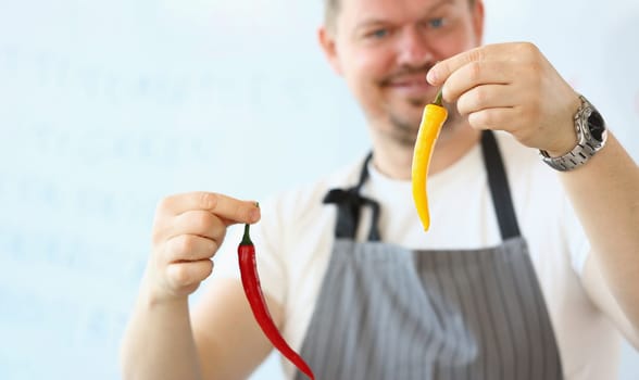 Cook is holding red and yellow hot chili peppers. Hot peppers are good for health