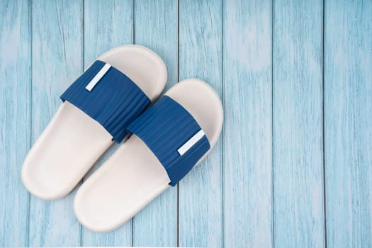 Top view of white and blue color rubber slipper shoes on blue wooden background with copy space. Summer holiday vacation concept.
