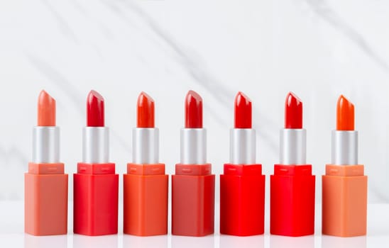 Multicolored color lipsticks arranged in line on white marble background.