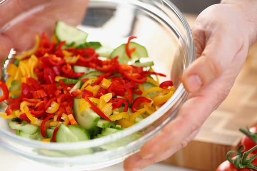 Sliced colorful vegetables in glass salad bowl. Cucumbers with yellow and red peppers in a salad