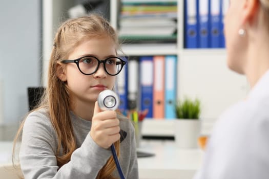 Girl child on medical examination holds stethoscope. Smiling child trusts doctor pediatrist