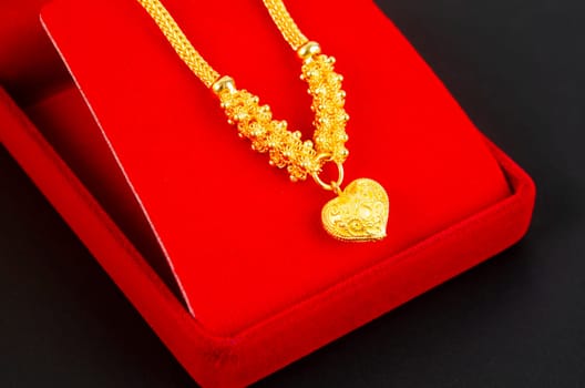 Gold necklace and heart shape pendant and gold ring on red velvet box.