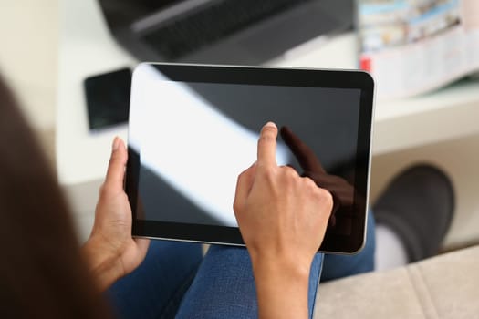 Woman hand holds tablet at home and controls finger across screen. Woman surfing internet using an app