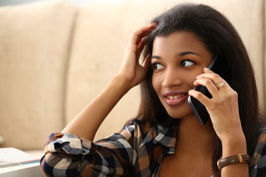 Smiling pensive young black woman talking on phone in living room. Talking on phone and discussing news