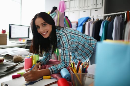Smiling woman stylist designer seamstress draws clothes sketch. Creation of creative fashion collection of clothes