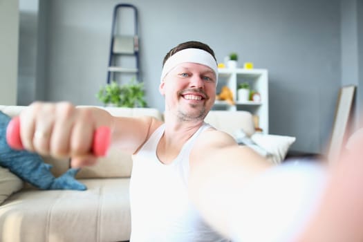 Emotional happy excited young man posing with dumbbells and taking selfie. Athlete man doing exercises with dumbbells at home