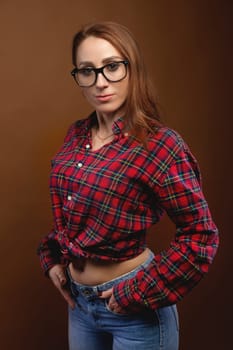 Smiling brunette in glasses posing with her hands down, in jeans and looking at the camera on a colored background, photo studio.