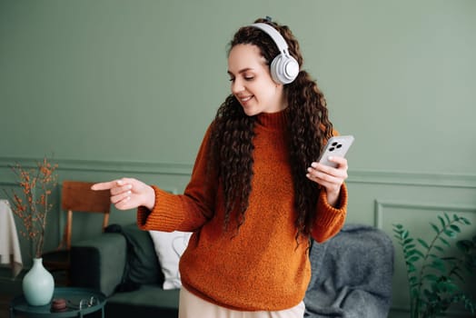 Enjoying the beats: woman dancing to music on phone with headphones in living room. Happy woman dancing while listening to music on smartphone with headphones