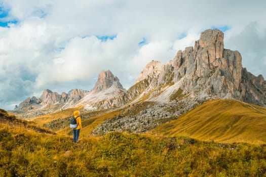Tourist in yellow jacket and backpack enjoying the exploration amidst the towering mountains of the famous Giau Pass.