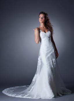 Beautiful slim bride posing in elegant long dress, on gray background