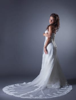 Slender brunette posing in stylish wedding dress, on gray background