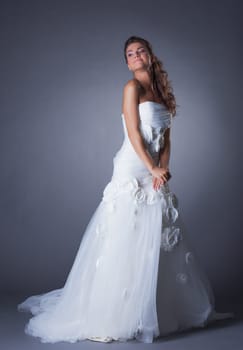 Dreamy brunette posing in elegant wedding dress, on gray background