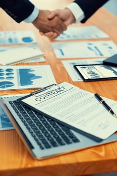 Closeup professional businessman shaking hands over desk in modern office after successfully analyzing pile of dashboard data paper as teamwork and integrity handshake in workplace concept. fervent