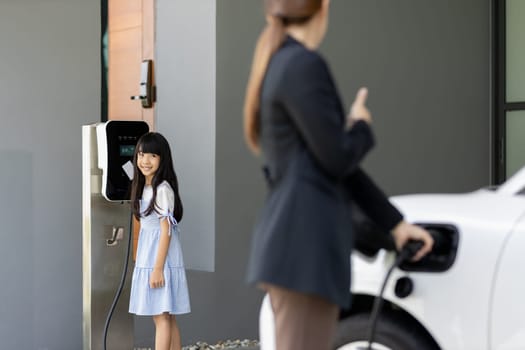 Progressive lifestyle of mother and daughter who have just returned from school in an electric vehicle that is being charged at home. Electric vehicle powered by sustainable clean energy.