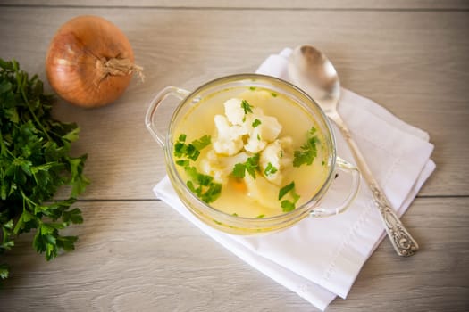 cooked chicken soup with cauliflower and vegetables in a bowl on a wooden table