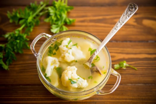 cooked chicken soup with cauliflower and vegetables in a bowl on a wooden table