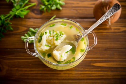 cooked chicken soup with cauliflower and vegetables in a bowl on a wooden table