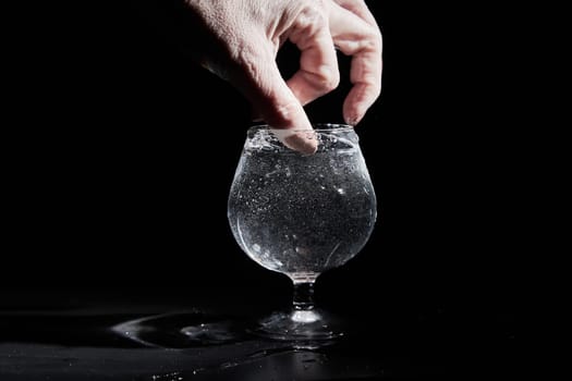 Fingers of hand of a woman touching water or mineral water in a wine glass on black background