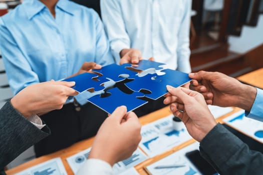 Corporate officer worker collaborate in office, connecting puzzle pieces with report paper on table as partnership and teamwork. Unity and synergy in business concept by merging jigsaw puzzle. Concord