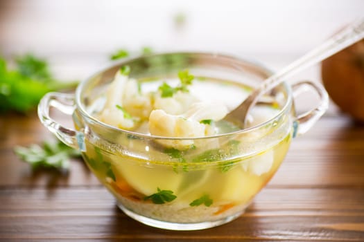 cooked chicken soup with cauliflower and vegetables in a bowl on a wooden table